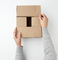 twee vrouw handen dichtbij een plein bruin karton doos Aan een wit achtergrond foto