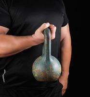 volwassen sterk atleet in zwart kleren Holding een ijzer kettlebell Aan zijn uitgestrekt armen foto