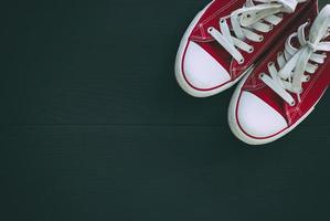 paar- van rood sportschoenen jeugd Aan een zwart houten achtergrond, leeg ruimte foto