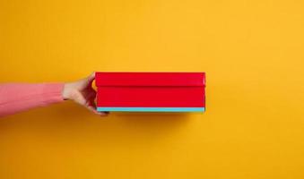 vrouw hand- Holding een rood karton doos Aan een geel achtergrond, levering foto