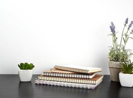 stack van spiraal notebooks met wit Pagina's en keramisch potten met planten Aan een zwart tafel foto