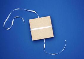 Gesloten karton geschenk plein doos gebonden wit dun lint Aan een donker blauw achtergrond foto