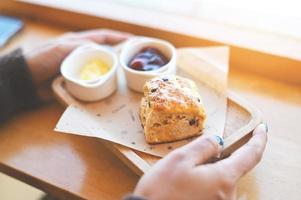 scones en jam Aan houten bord, vrouw geserveerd scones en room voor toetje en thee - vers eigengemaakt boter scones foto