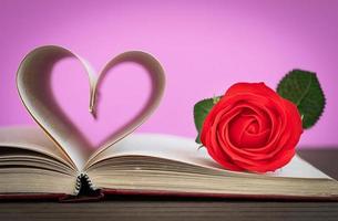bladzijde van boek gebogen hart vorm en rood roos foto