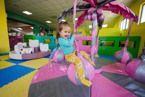 gelukkig meisje spelen Bij binnen- Speel centrum speelplaats, schommel Aan palm. foto
