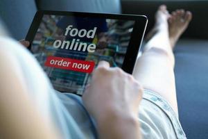 Dames gebruik tablets naar bestellen voedsel online terwijl aan het liegen Aan de bankstel Bij huis. foto
