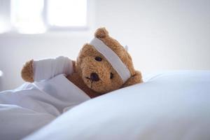 teddy beer aan het liegen ziek in bed met een hoofdband en een kleding gedekt foto