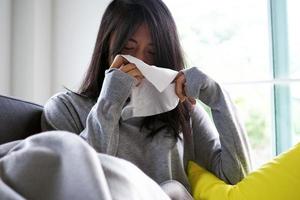 Aziatisch vrouw niezen in zakdoek. ziekte, aan het liegen Aan de sofa foto