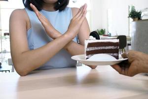 een van de gezondheidszorg meisjes gebruikt een hand- naar Duwen een bord van chocola taart. weigeren naar eten voedingsmiddelen dat bevatten trans dik. foto