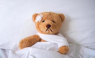 de teddy beer viel ziek in de bed, gewond door de ongeluk. verzekering concept foto