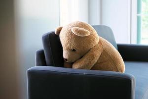 de concept van rouw van kinderen. de teddy beer zit Aan de bankstel binnen de huis, alleen op zoek verdrietig en teleurgesteld. foto