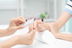 vrouw te ontvangen zorg onderhoud door professioneel schoonheidsspecialist manicure Bij spa centrum. nagel schoonheid salon gebruik nagel het dossier voor beglazing behandeling. manicure maken nagel klant naar mooi. lichaam zorg spa behandeling foto