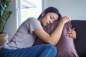 de vrouw is knuffelen de hoofdkussen Aan de sofa binnen de huis. in een verdrietig, deprimerend manier, denken moeilijk over de probleem. foto