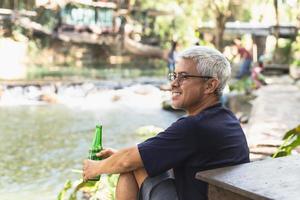 gelukkig Mens met glimlach hand- Holding fles van bier met nuture buitenshuis. foto