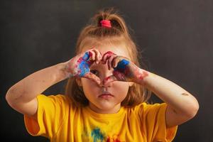 detailopname weinig meisje gevouwen haar vingers in de vorm van een hart, haar handen in veelkleurig holi kleuren, een teken van liefde. Indisch festival van kleuren holi. foto