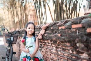 schattig klein Aziatisch meisje in jurk met een rode roos in het park foto