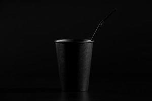 zwart papier glas met een buis op een zwarte achtergrond. een glas koffie of thee met een plastic deksel foto