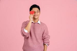 portret van blij knap Aziatisch Mens Holding rood papier hart over- ogen, met kopiëren ruimte. foto