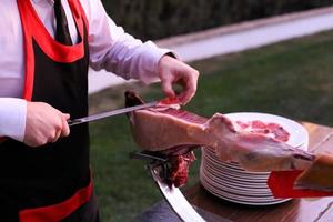 een persoon die een stuk ham snijdt op een Iberisch gerecht. foto