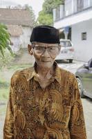 een portret van een oud Aziatisch Mens vervelend batik overhemd en bril foto