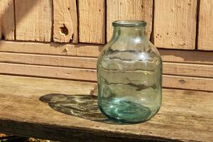 leeg glas kan. een drie liter pot staat Aan een houten bank in de buurt de huis. foto