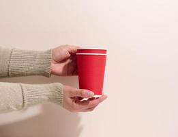 hand- houdt papier karton rood cups voor koffie, beige achtergrond. milieuvriendelijk servies, nul verspilling foto