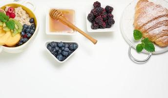bord met havermout en fruit, voor de helft een rijp oranje en vers geperst sap in een transparant glas karaf, honing in een kom Aan een wit tafel. gezond ontbijt foto