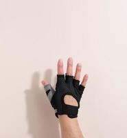 zwart sport- handschoen Aan een vrouw hand, beige achtergrond. een deel van de lichaam is opgeheven omhoog foto