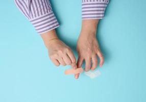 vrouw hand- en bruin medisch Zelfklevend gips voor de behandeling van verwondingen en bezuinigingen Aan de huid, blauw achtergrond foto