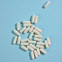medisch poeder in wit capsules Aan een blauw achtergrond. behandeling pillen, voedingswaarde supplementen foto