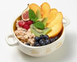 gekookt havermout met fruit in een ronde bord Aan een wit tafel, gezond ontbijt foto