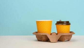 twee oranje papier beschikbaar cups staan in een bruin dienblad Aan een blauw achtergrond foto