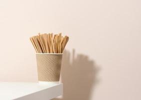 bruin papier karton cups en houten roeren stokjes Aan een wit tafel, beige achtergrond. milieuvriendelijk servies, nul verspilling foto