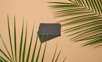 een stack van rechthoekig zwart papier bedrijf kaarten en een blad van een palm boom Aan een bruin achtergrond. visie van bovenstaand foto