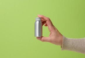 vrouw hand- Holding een zilver metaal fles voor schoonheidsmiddelen Aan een groen achtergrond foto