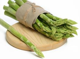 bundel van vers asperges verpakt in bruin papier leugens in een houten bord foto