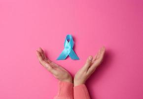 vrouw handen Holding licht blauw lint bewustzijn Aan een roze achtergrond. Mannen Gezondheid en prostaat kanker bewustzijn campagne concept. foto