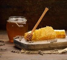 was- honingraat met honing Aan een houten bord, achter een pot van honing foto
