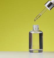 essentieel olie vallend van de amber glas druppelaar. wit fles van kunstmatig olie met een pipet, groen achtergrond foto