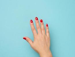 vrouw hand- met rood manicure verheven omhoog Aan een blauw achtergrond foto