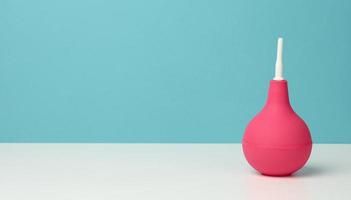 roze rubber klysma Aan wit tafel, medisch instrument voor schoonmaak de lichaam, blauw achtergrond foto