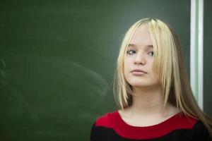 hoog school- leerling. een tiener- meisje staat tegen de achtergrond van een schoolbord en looks in de camera. foto