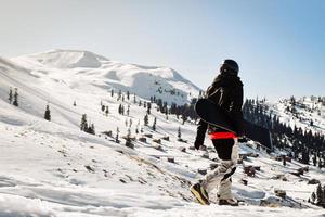 mannetje snowboarder gekleed in donker zwart sportkleding wandelen genieten keer bekeken panorama van oud gebouwen naar beneden de berg helling in Georgië, goderdzi Aan Kaukasus zonnig dag foto