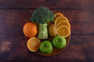 stukjes sinaasappel met appel, kiwi en broccoli op een houten plaat foto