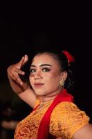 een scherp blik van een Indonesisch vrouw met bedenken Aan haar gezicht terwijl vervelend een oranje jurk en gouden oorbellen foto
