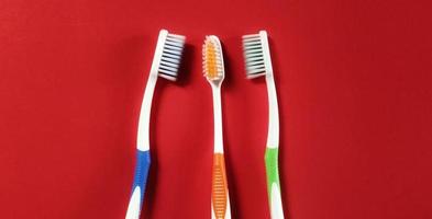 drie verschillend gekleurde tandenborstels geïsoleerd Aan rood achtergrond. bovenaanzicht foto