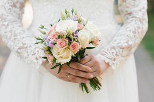 de handen van een jong bruid zijn Holding een mooi delicaat bruiloft boeket. bruid hand- met een bruiloft ring Aan haar vinger. bruid in wit jurk foto