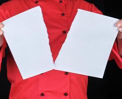 Mens in een rood uniform houdt een wit vel van papier gescheurd in voor de helft foto