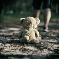 bruin teddy beer zit terug in de midden- van een zanderig weg in de Woud foto