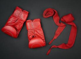 paar- van rood leer boksen handschoenen en rood textiel verband Aan een zwart achtergrond foto